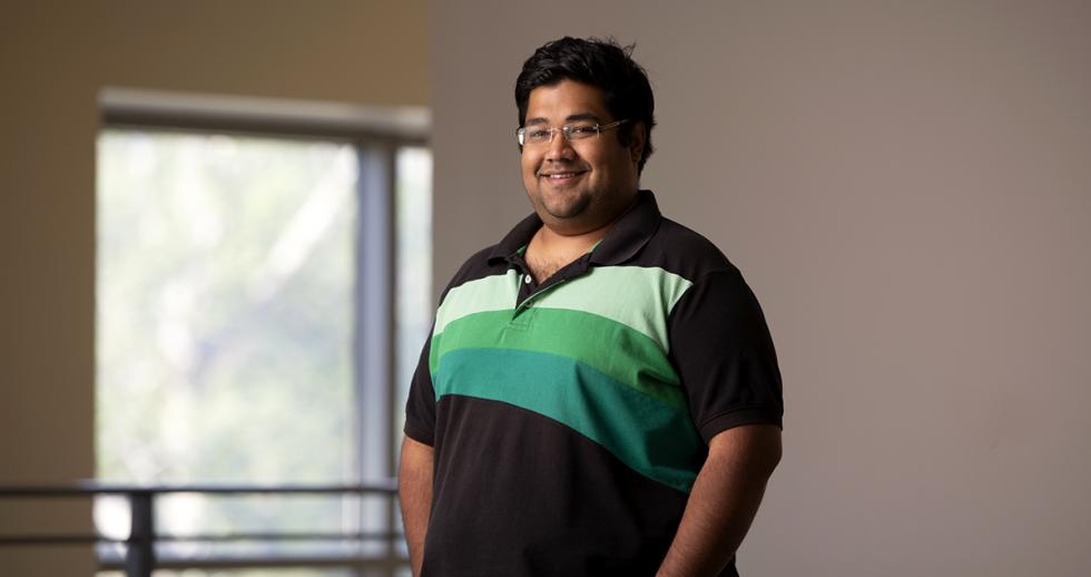 male postdoc wearing striped shirt and standing in academic building