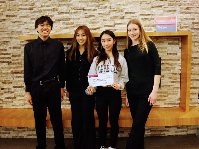 Four students stand together holding a large check at the Little Bang competition