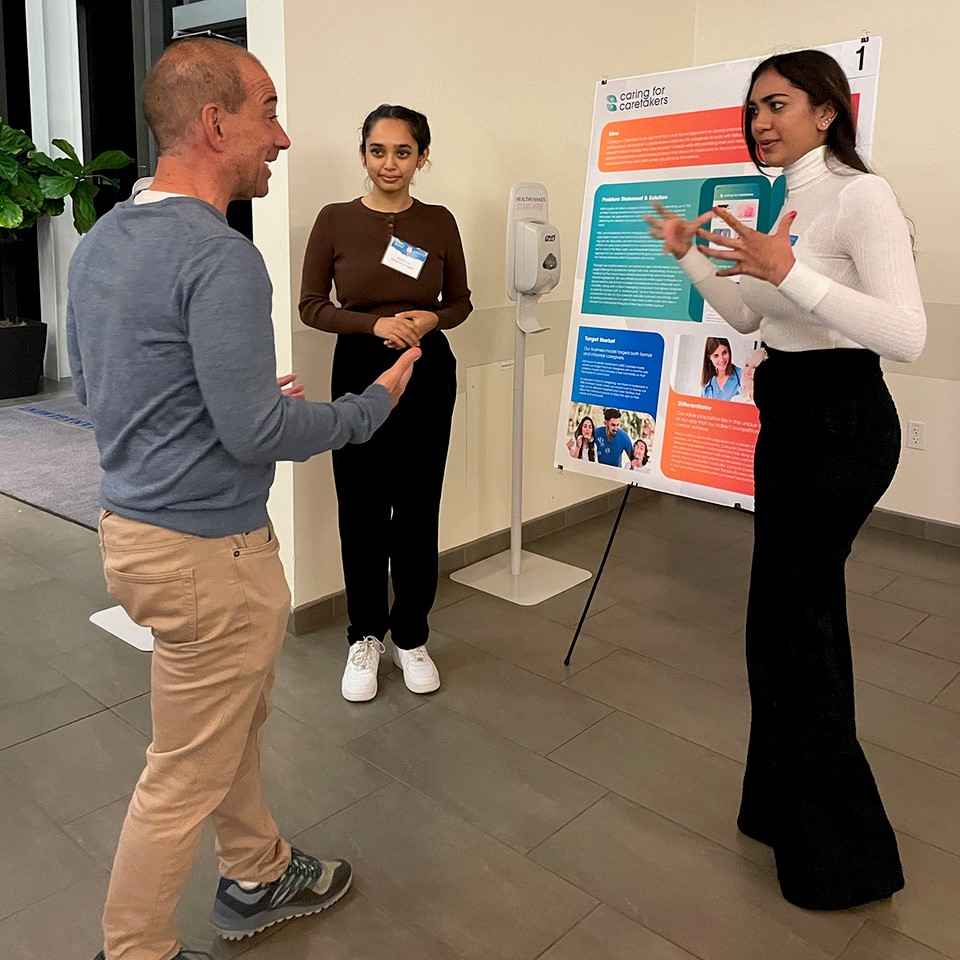 photo of a man discussing business competition poster with two women students