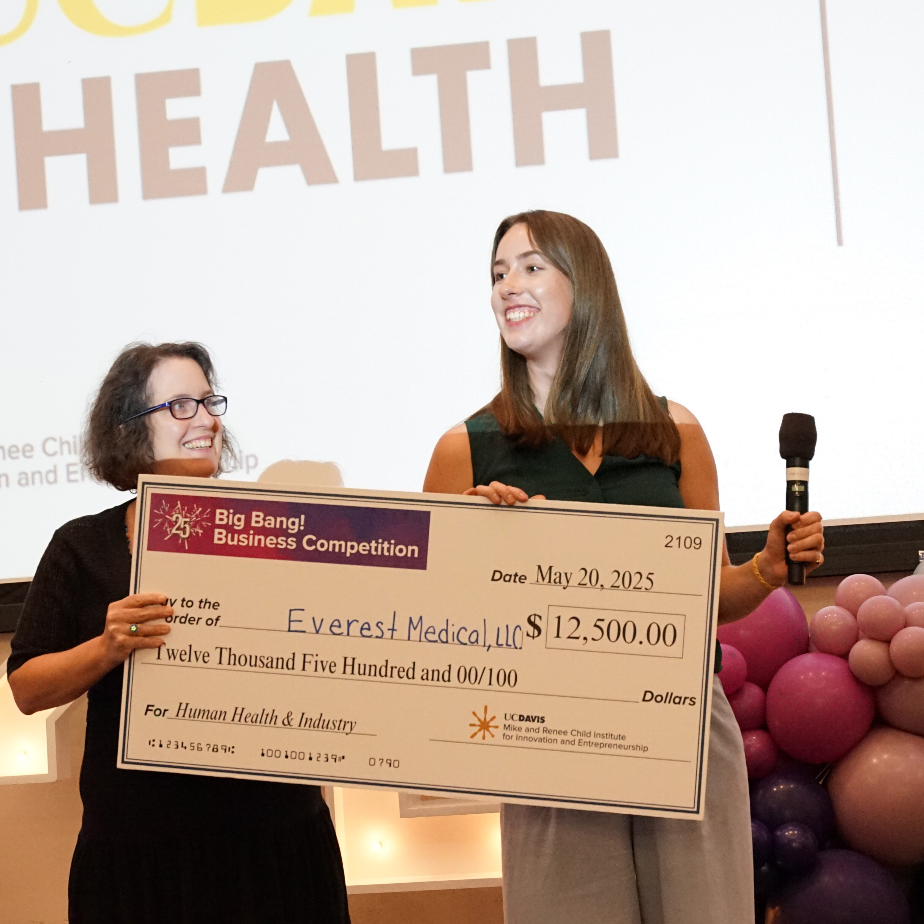 Two people standing on stage holding a large check made out to Everest Medical, LLC