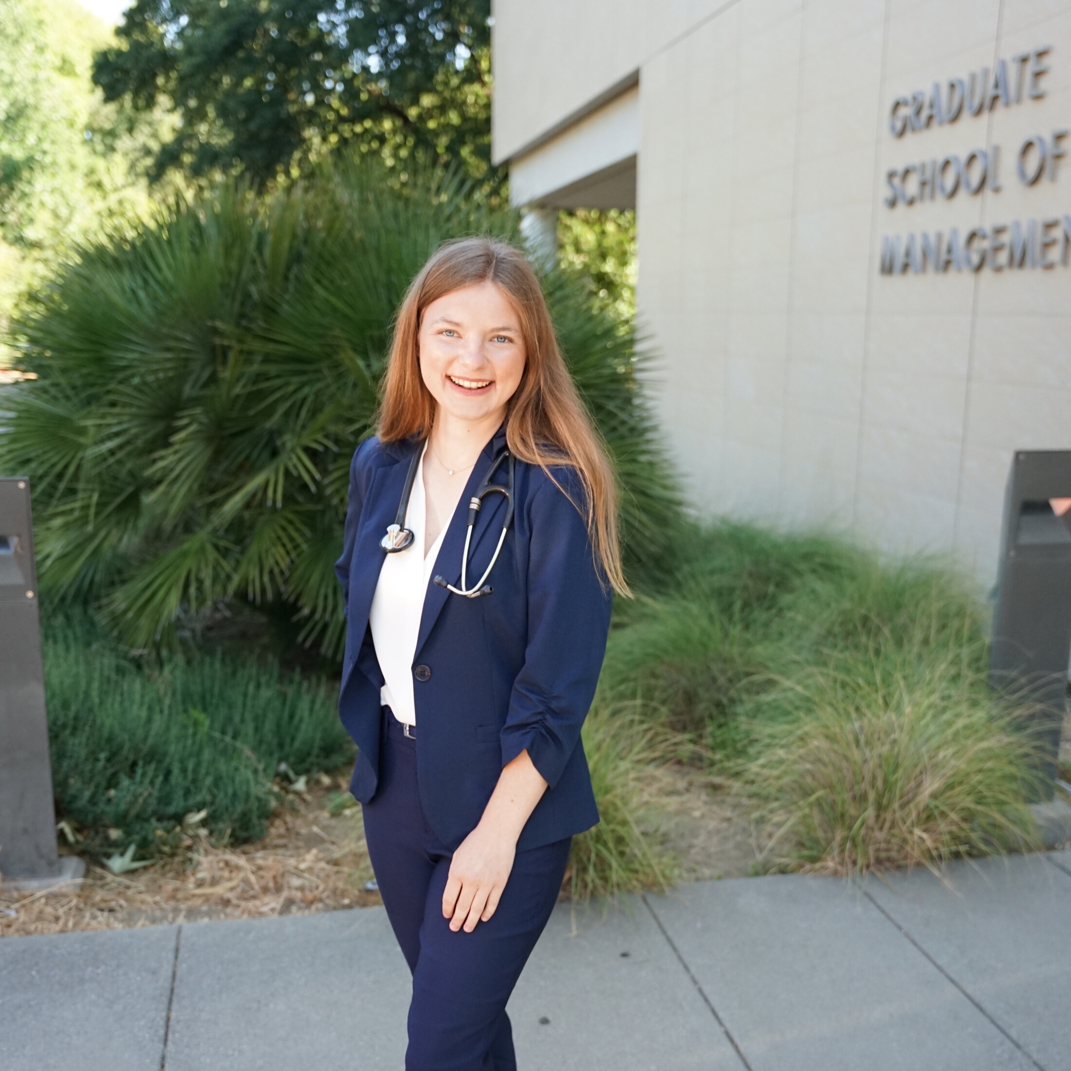 female vet student stands in front of Gallagher Hall, she is wearing a stethoscope around her neck