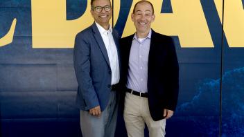 two men in business attire standing in front of a wall that has text: UC Davis