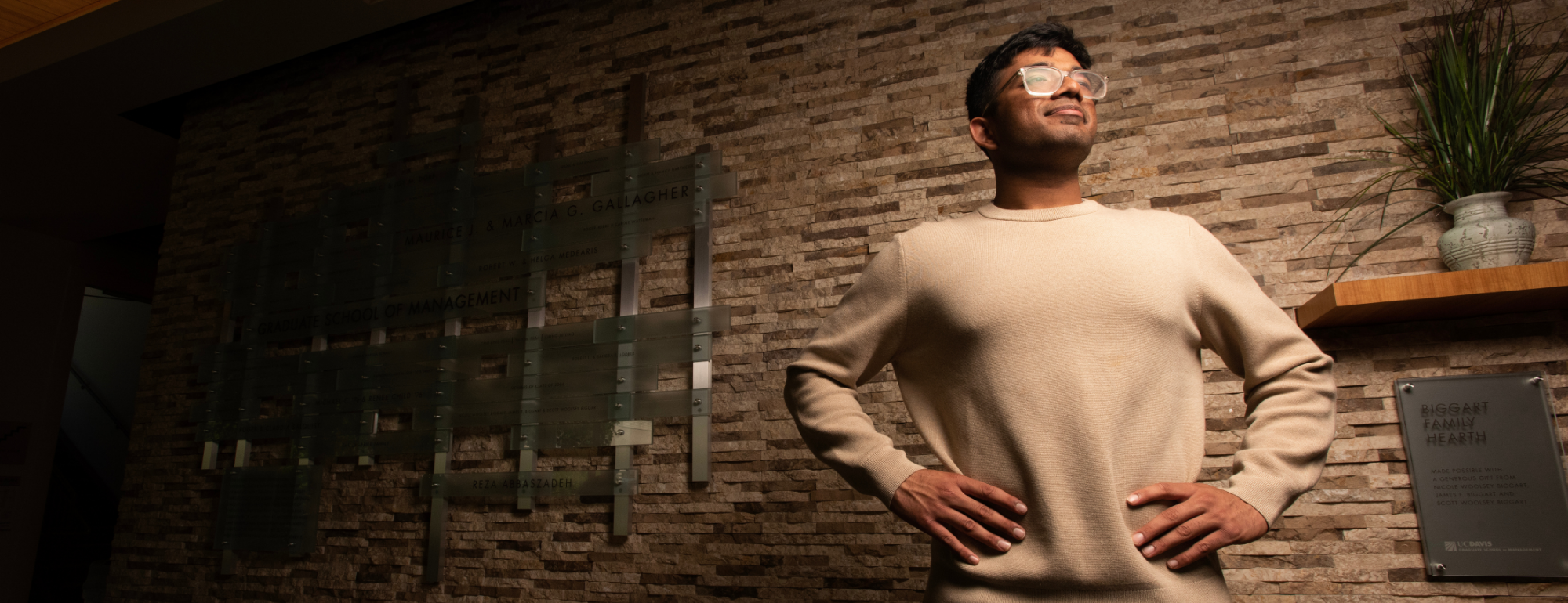 Mn with glasses in beige sweater stands hands-on-hips, gazing up.