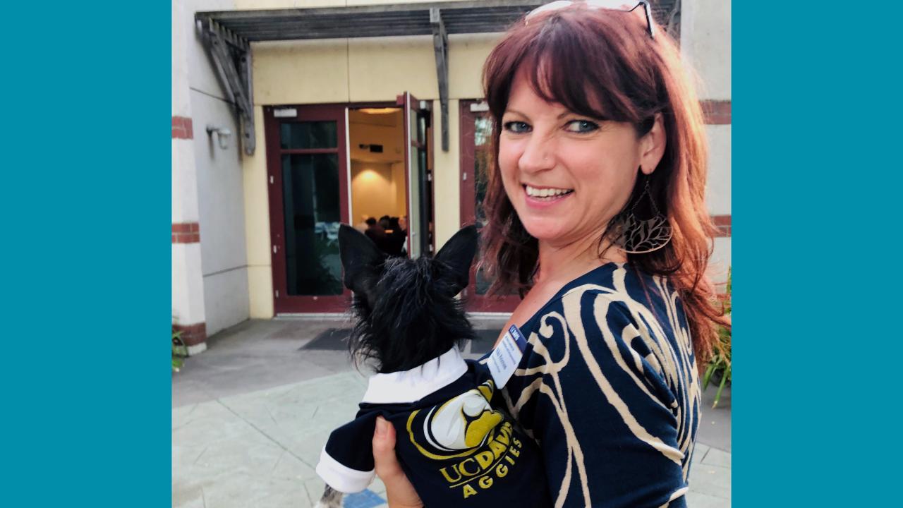 woman outdoors holding small dog wearing aggies logo outfit