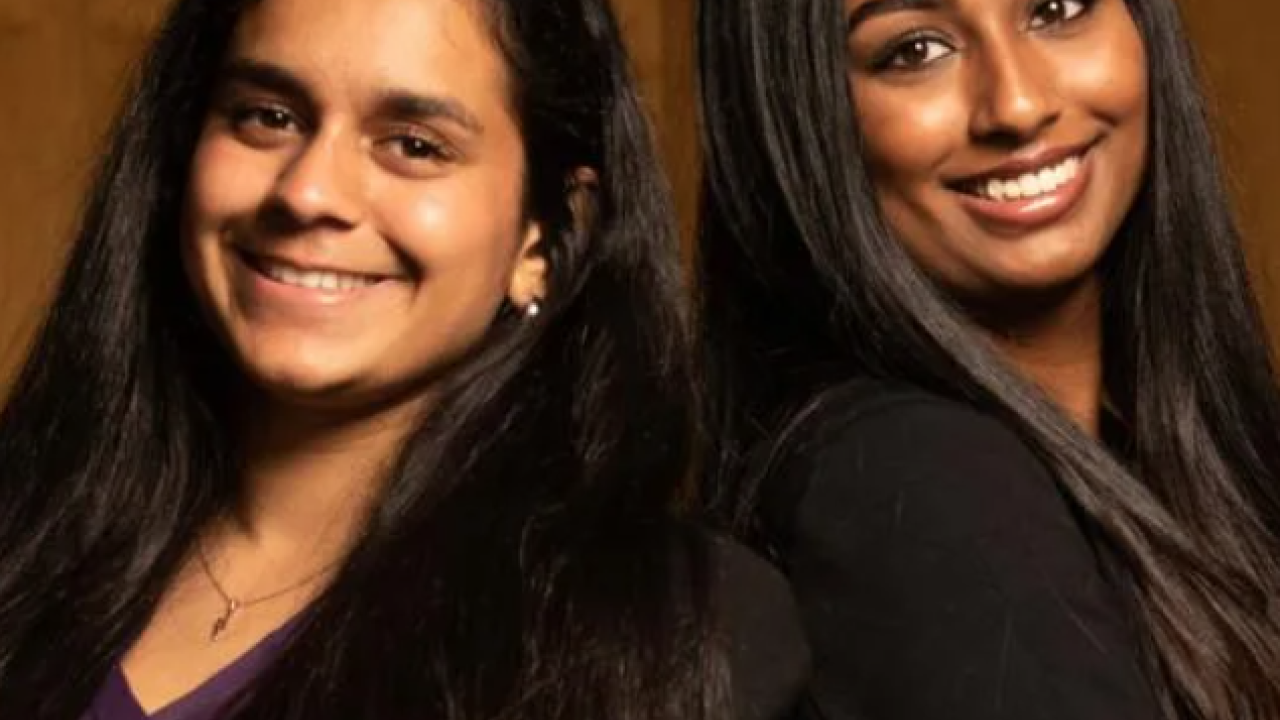 Simran Lallian and Jaya Athuluru pose back to back against a brown background.