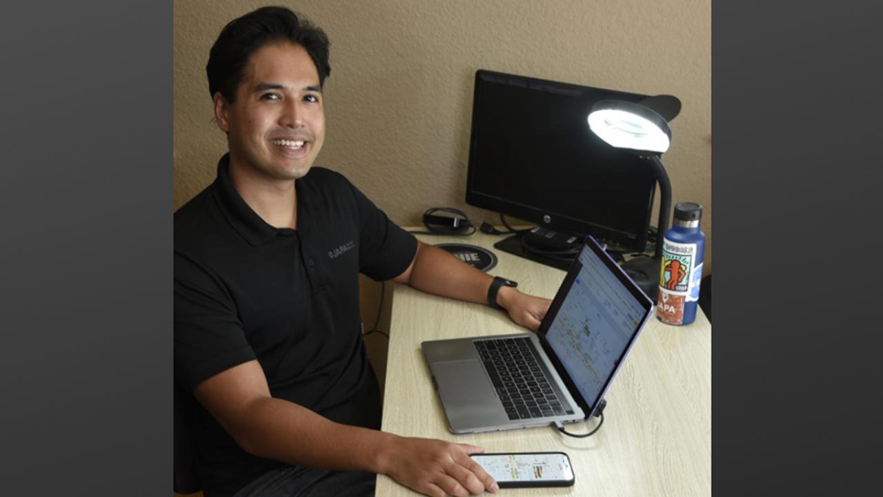 image of one male sitting at desk indoors with computer and phone app on display