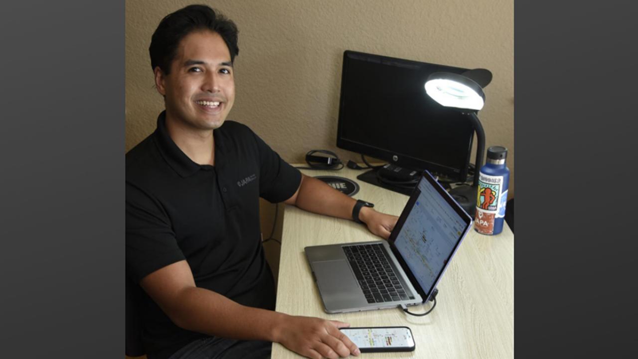 image of one male sitting at desk indoors with computer and phone app on display