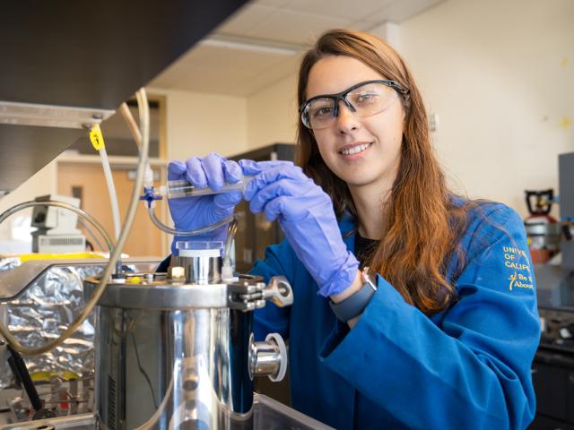 photo of a woman graduate student in her lab, wearing blue lab coat