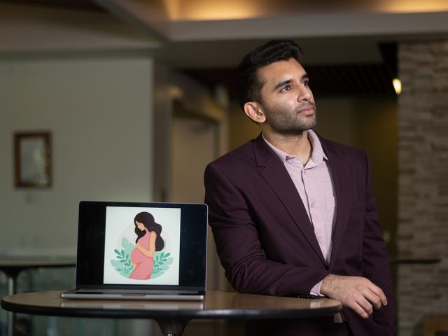 photo of a young man in a suit next to a laptop opened to his startup's logo