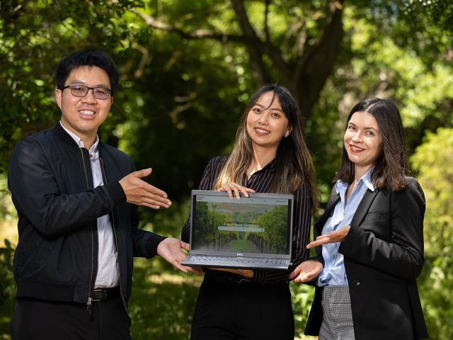 photo of three people standing outdoors with a laptop open to an image of winegrapes