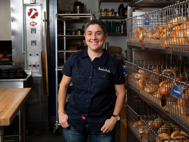 Emily Winston stands beside a rack of bagels at Boichick bagels. 