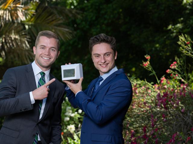 photo of two young men with a prototype of their medical device, standing outdoors