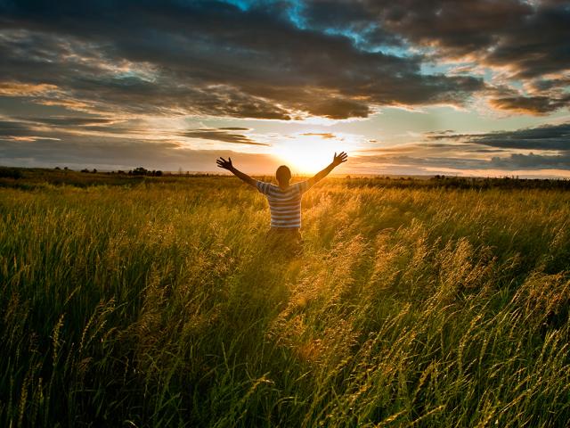 photo of man in field at dawn with arms stretching up and out