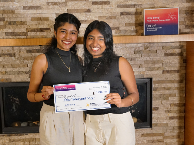 two students stand together and hold a little bang check