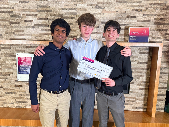 three students standing together, holding a check for the little bang competition
