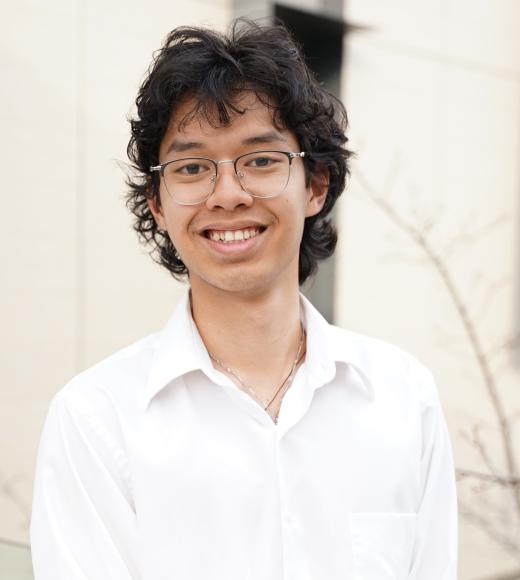 A headshot of a young man with curly hair and glasses, smiling in a light-colored shirt against a neutral background.