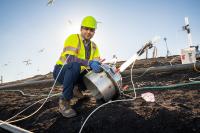 photo of a man wearing bright yellow vest and hardhat, in a field with equipment