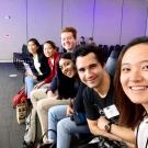 Students smiling in chairs against purple wall