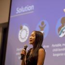 woman with microphone pitching her startup with large graphic behind her