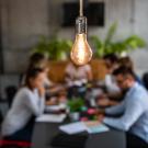 photo of a lightbulb with soft focus table of young entrepreneurs in the background