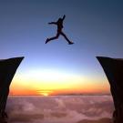 person jumping between two cliffs with sunrise and clouds in the background