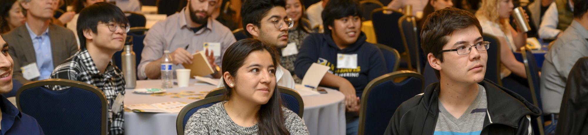 Undergraduate students at conference sitting around tables listening to speaker.