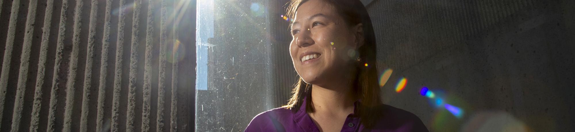 woman standing outside with buildings in background and the glare of sun lighting her face