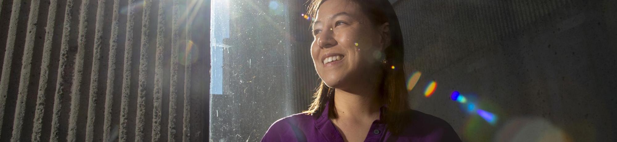 woman standing outside with buildings in background and the glare of sun lighting her face