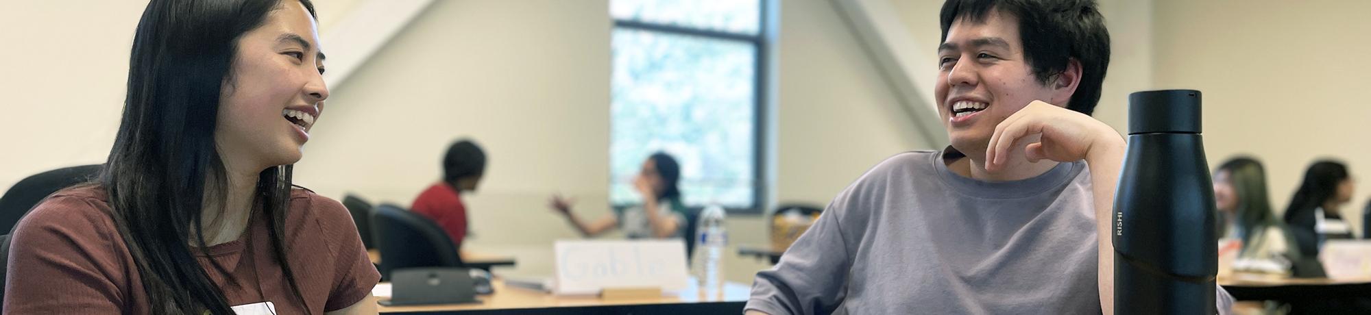 two undergraduates at a classroom table talking